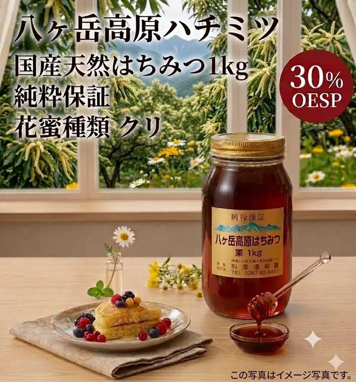 木のテーブルの上には、ベリーをトッピングしたパンケーキの皿の横に、スプーンが添えられた「八ヶ岳高原 国産天然はちみつ 1kg 純粋保証 花蜜の種類：クリ」の瓶が置かれている。画像には、日本語の文字と「OESP 30%」と記された赤いラベルが見える。.